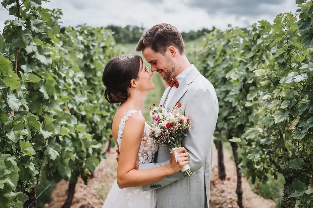 Brautpaar schaut sich einander verliebt in zwischen den Weinreben in den Weinbergen bei Weinstadt an. Himmel ist leicht bewölkt.